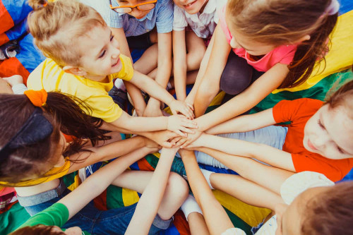 De nombreux enfants des deux sexes et du plus jeune âge se réunissent en cercle, habillés de couleurs vives, et posent leurs mains l'une sur l'autre