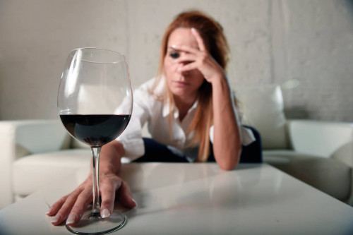 Une femme ivre avec des maux de tête est assise sur un canapé et touche un verre de vin rouge rempli