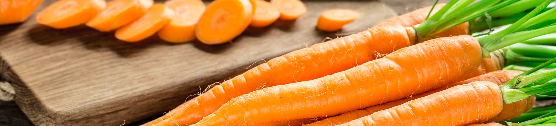 Carottes avec verdure sur une table en bois, à côté de carottes déjà coupées en rondelles sur une planche en bois