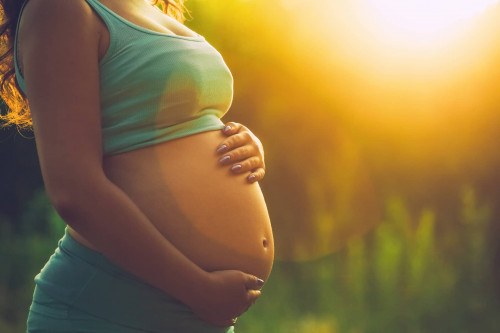 Détail du ventre de bébé dévêtu d'une femme qui lui impose les deux mains, avant le crépuscule